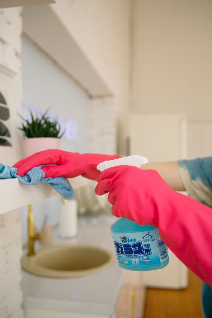 our-story Person using spray bottle and cloth for cleaning a kitchen shelf, ensuring hygiene and cleanliness.